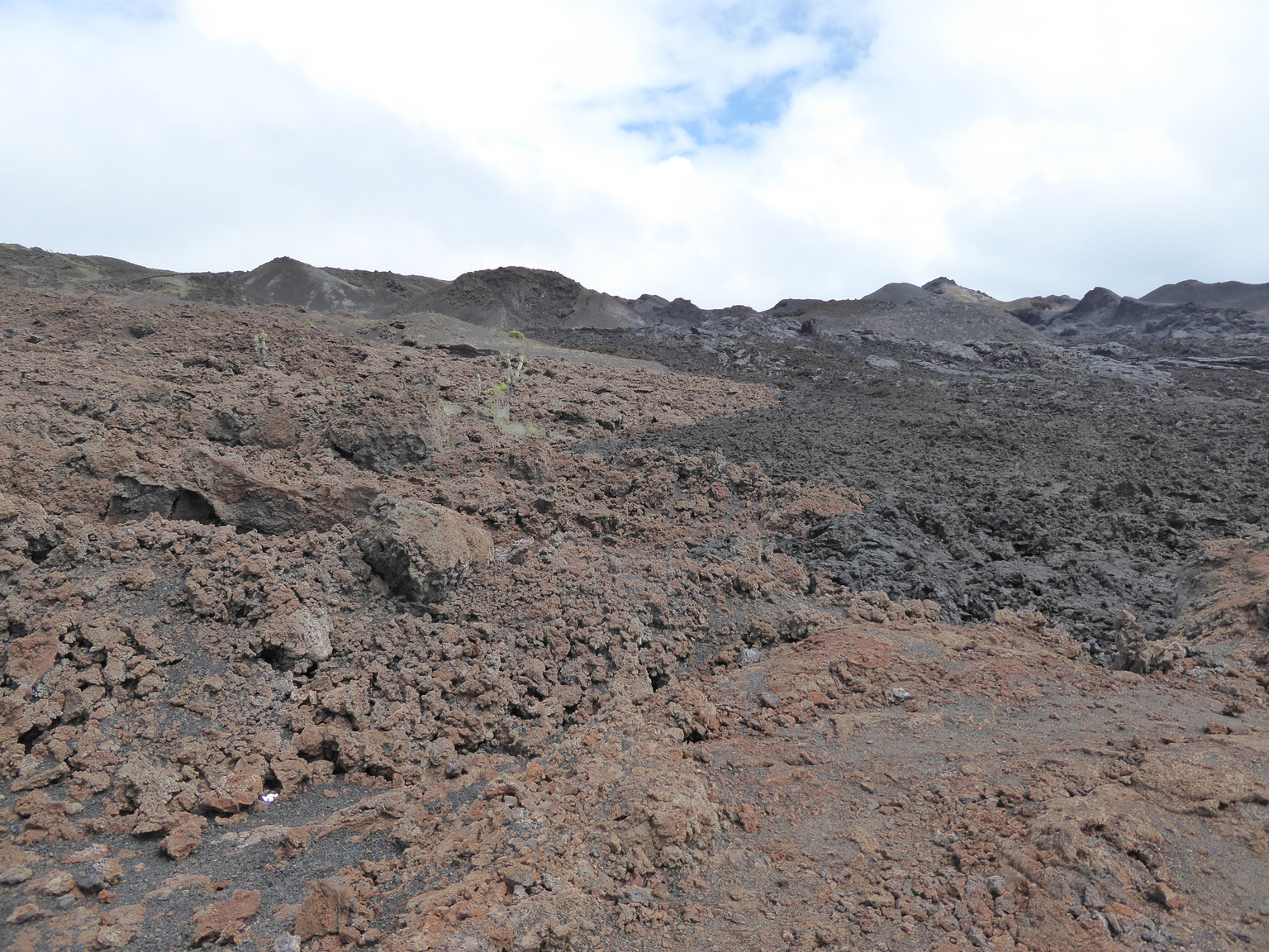 On the left the lava is older, oxidation has caused it to turn reddish-brown. On the right, you can see newer lava, which is closer to black.